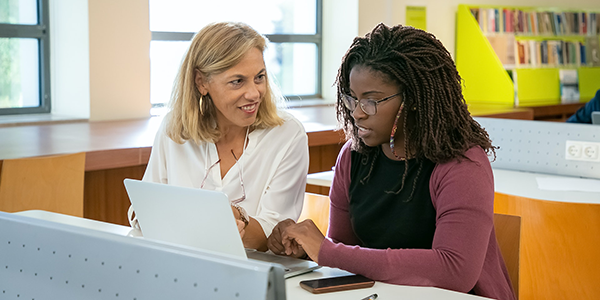 Student and teacher talking and looking at laptop